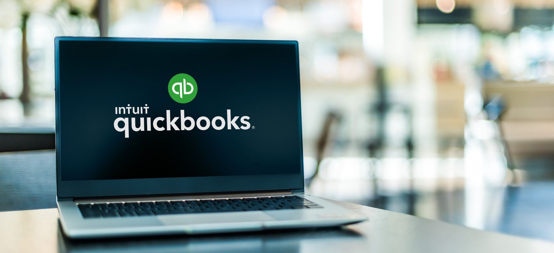 A laptop computer is sitting on a table with a quickbooks logo on the screen.