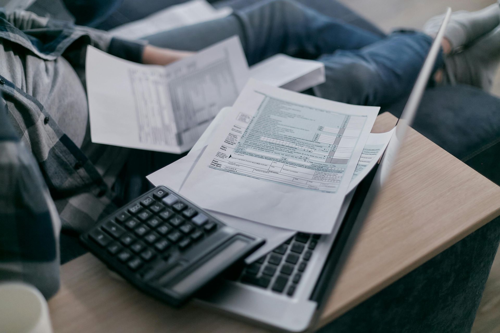 A person is sitting on a couch with a laptop and a calculator.