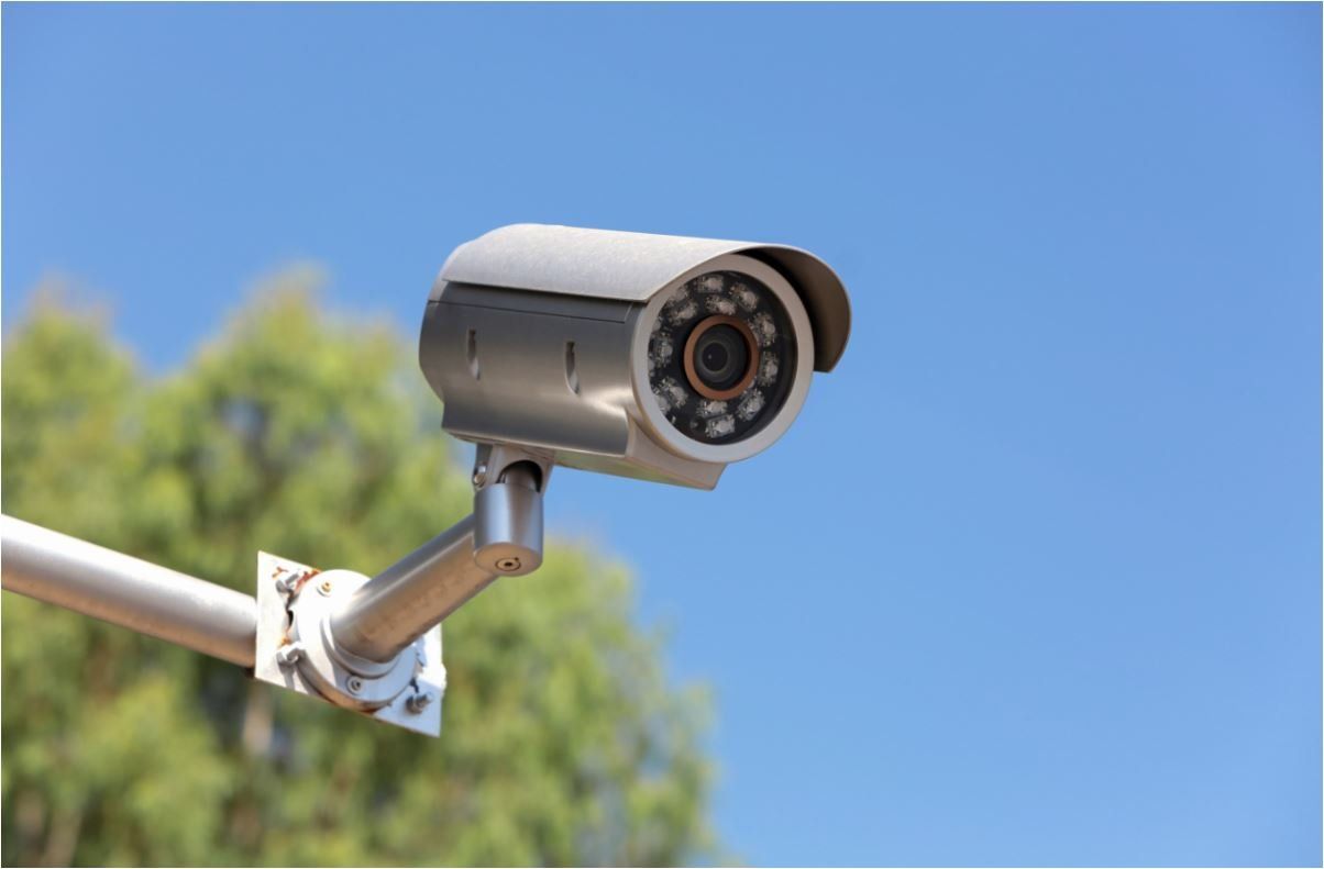 A CCTV camera in front of a tree and blue sky