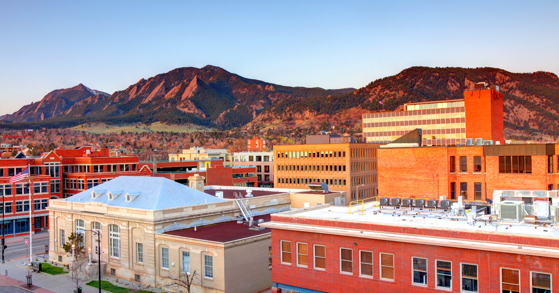 Downtown Boulder, Colorado, with red-brick buildings in the foreground and the sunlit Flatirons mountains in the back.
