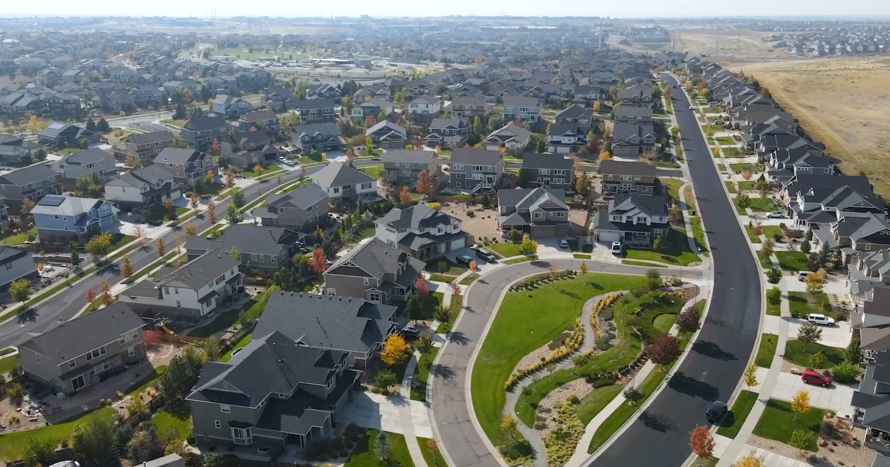 An aerial view of a sprawling suburban neighborhood featuring numerous houses, winding streets, and a central green space.