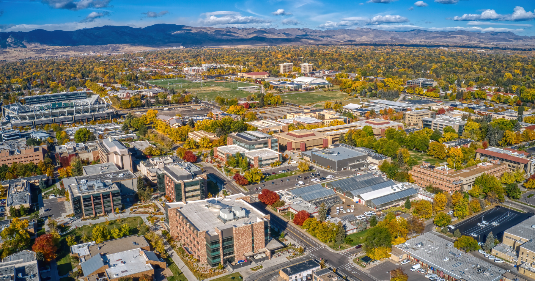 Aerial view of a sprawling college campus with autumnal trees, brick buildings, and distant mountains under a blue sky.