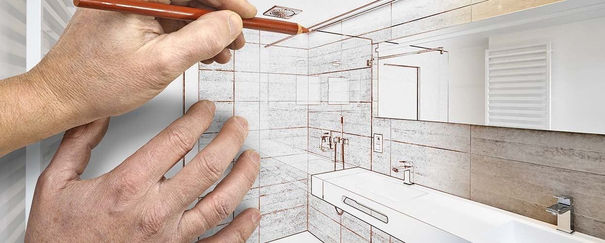 A hand uses a pencil to draw a blueprint overlay of a modern bathroom renovation onto an existing room.