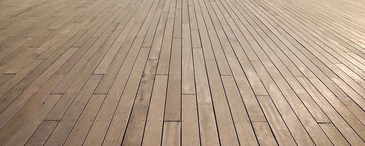 A low-angle view of a wooden boardwalk surface with parallel planks and regular spacing gaps, extending into the distance.