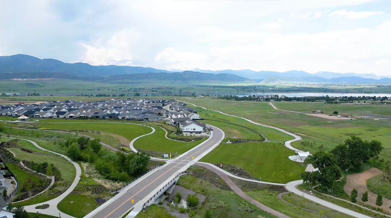 Aerial view of a residential neighborhood with green park space and paths, framed by mountains in the distance.