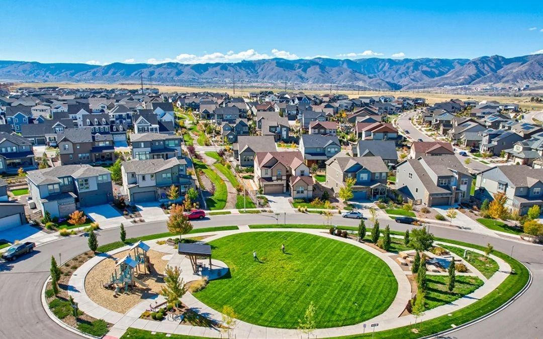 An aerial view of a circular community park with a playground, surrounded by suburban homes and mountains in the distance.