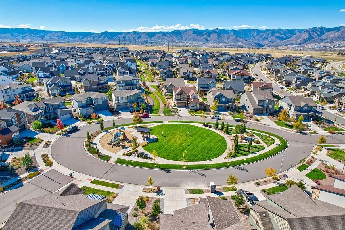 An aerial view of a suburban neighborhood centered around a circular park with green grass, landscaping, and a playground.