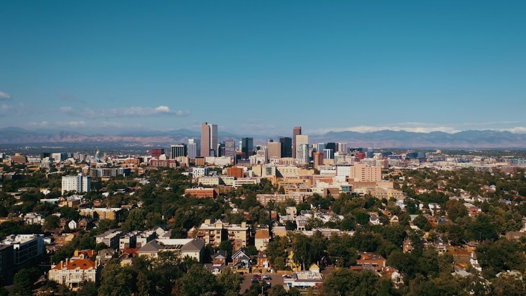 An aerial view of the Denver, Colorado city skyline featuring skyscrapers against a backdrop of distant mountains.
