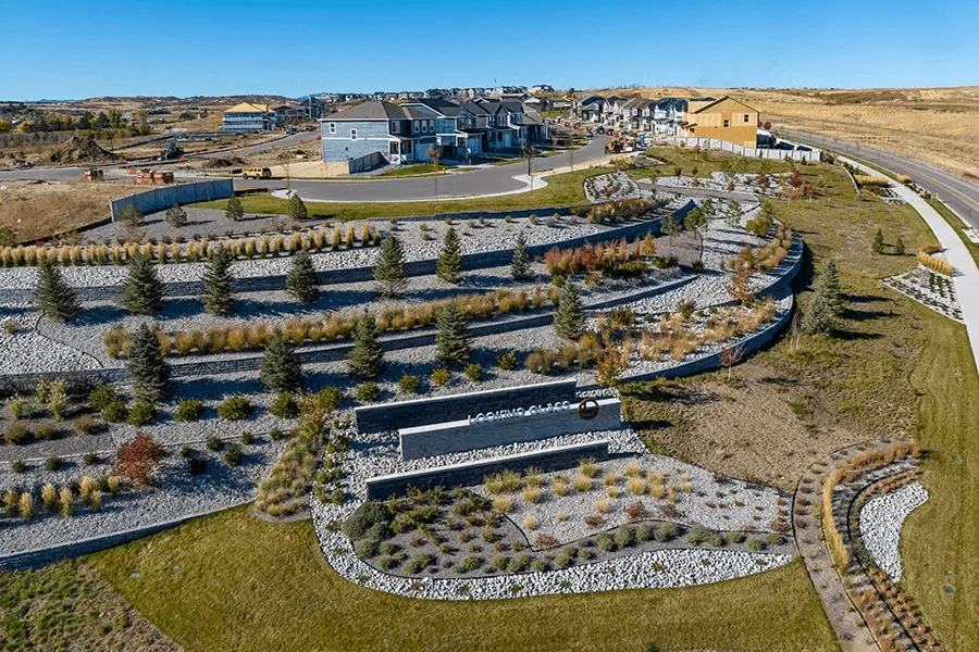 An aerial view of a terraced landscape with gravel, rows of small evergreen trees, and a low stone wall feature.