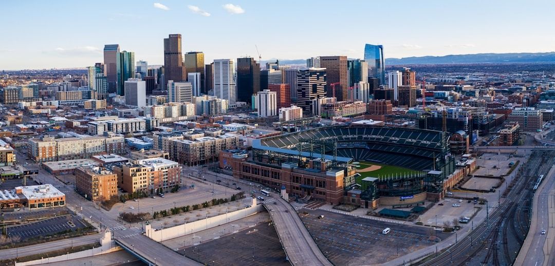 Aerial view of Denver, Colorado, featuring Coors Field in the foreground and the city skyline under a clear blue sky.