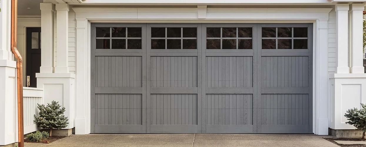 Gray garage door with four panels and windows, mounted in a white-trimmed residential exterior.