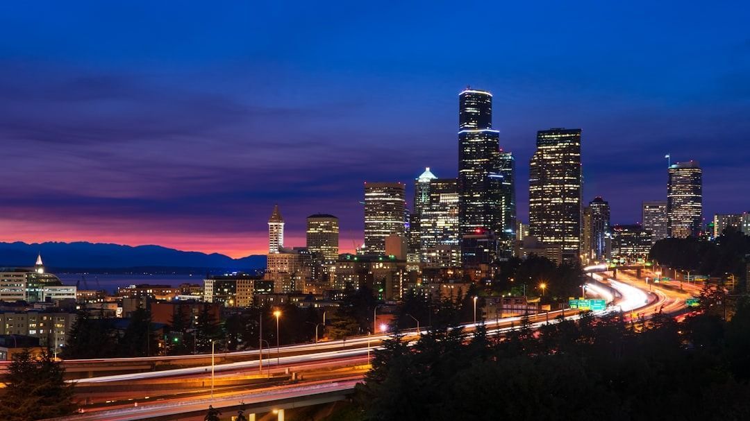 Seattle skyline at twilight with illuminated skyscrapers and light trails from traffic on the highway in the foreground.