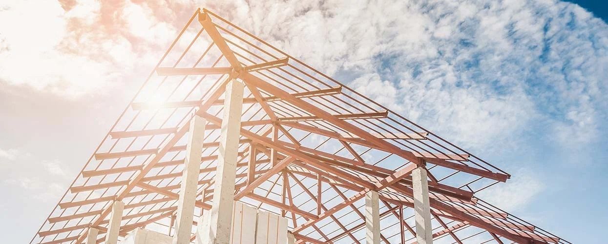 A partially constructed building frame with exposed steel beams against a bright, sunny sky.