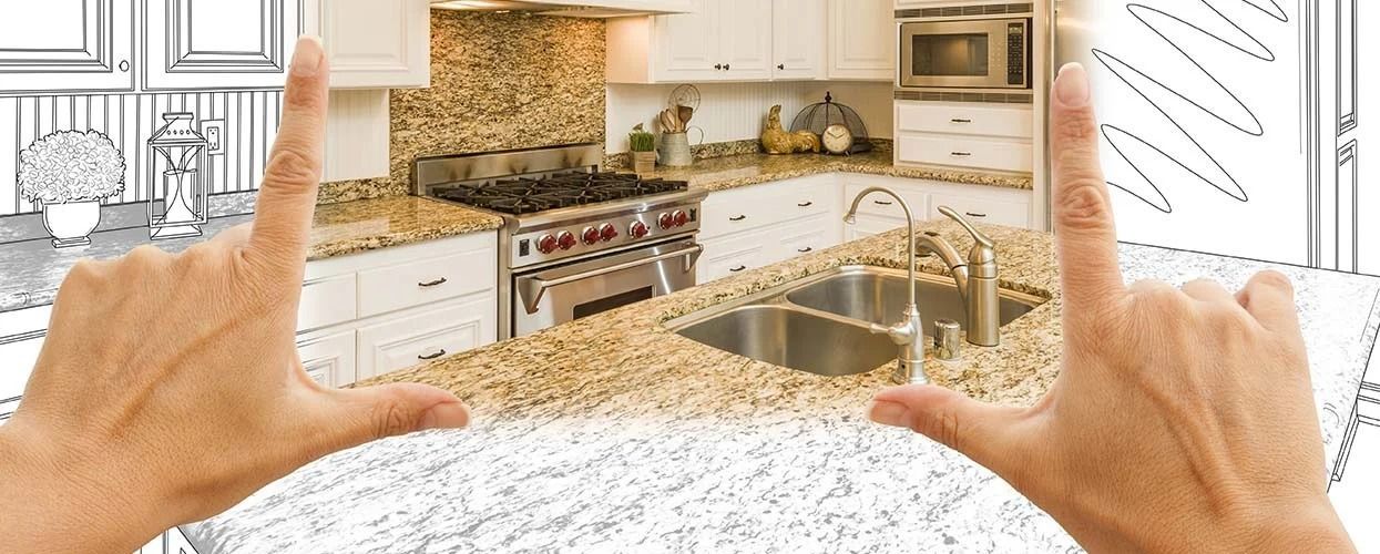 Hands forming a frame around a kitchen with white cabinets, granite countertops, and a stove.