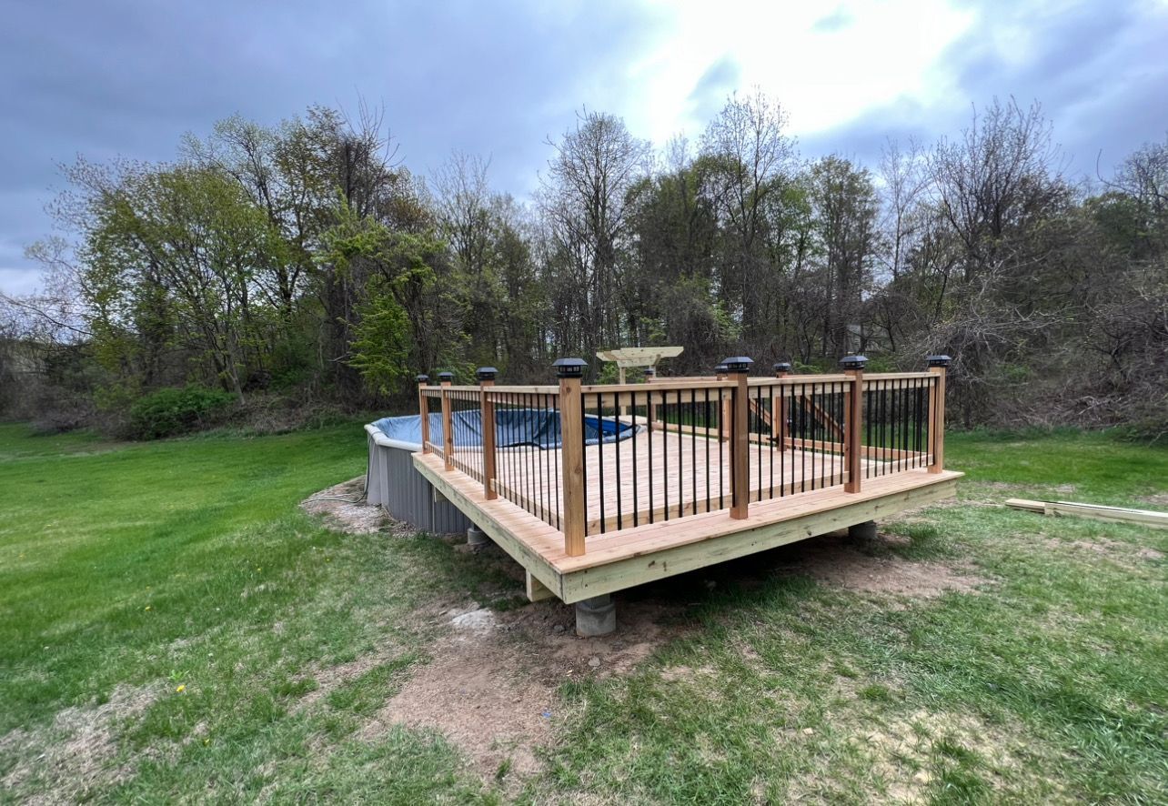 A wooden deck is sitting next to a pool in a backyard.
