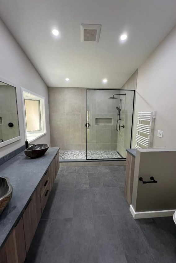 A bathroom with a walk in shower , sink , mirror and toilet.