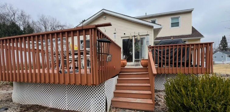 A large wooden deck with stairs leading to the back of a house.
