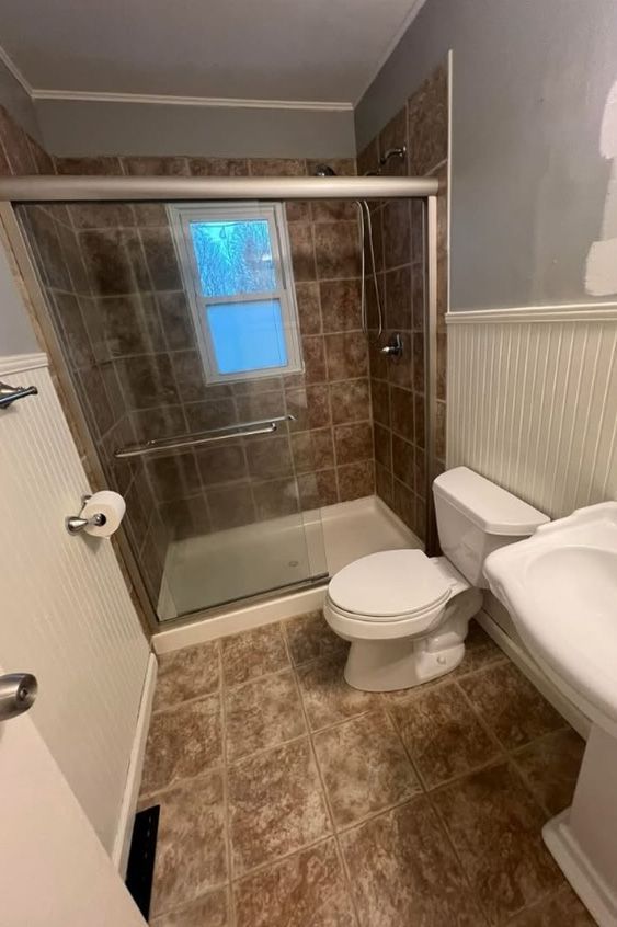 A bathroom with a toilet , sink , shower and window.
