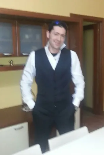 Un uomo in gilet e camicia bianca è in piedi in una stanza con le mani in tasca