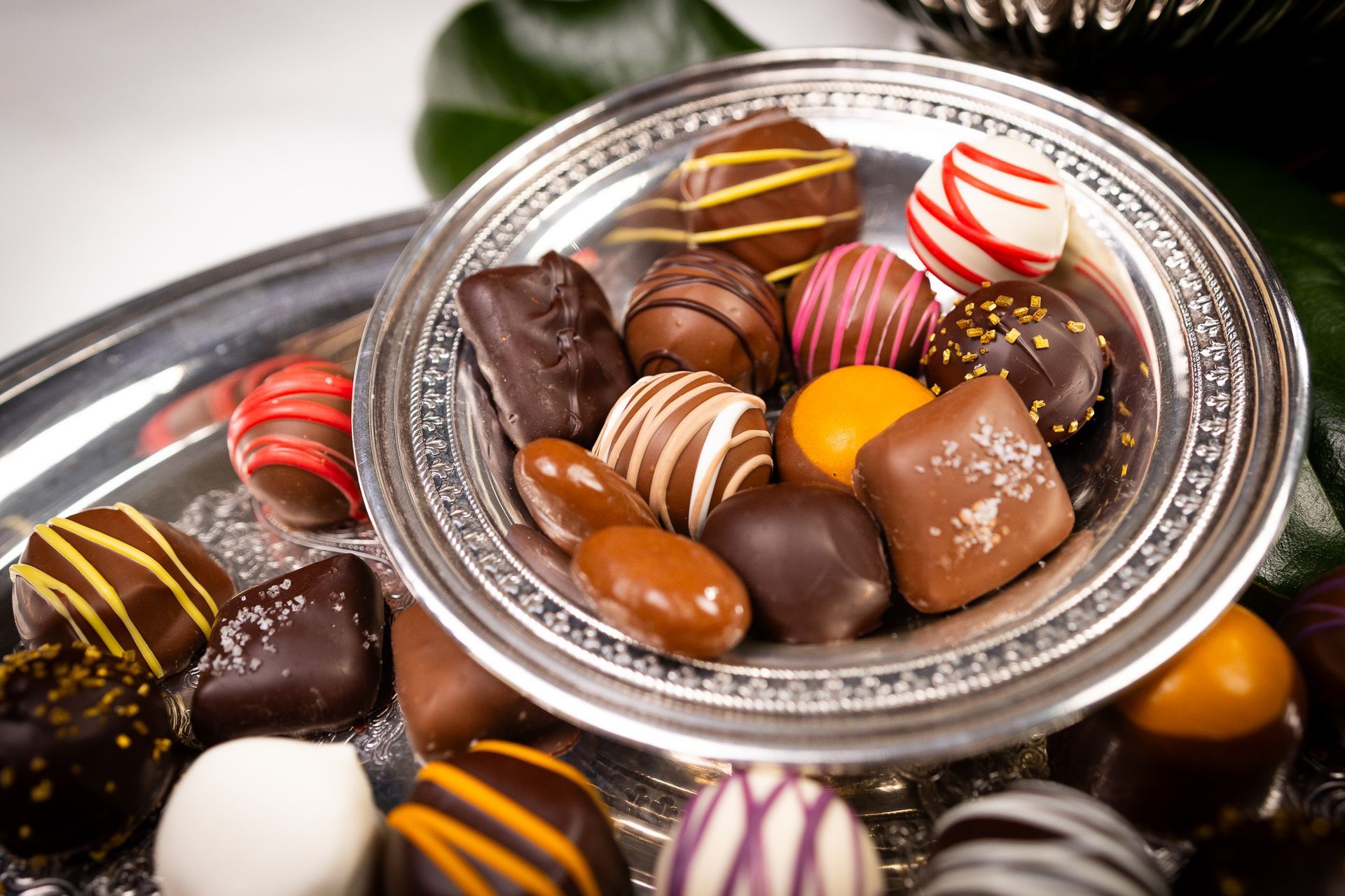 A silver bowl and serving platter filled with an assortment of colorful, decorated chocolates.