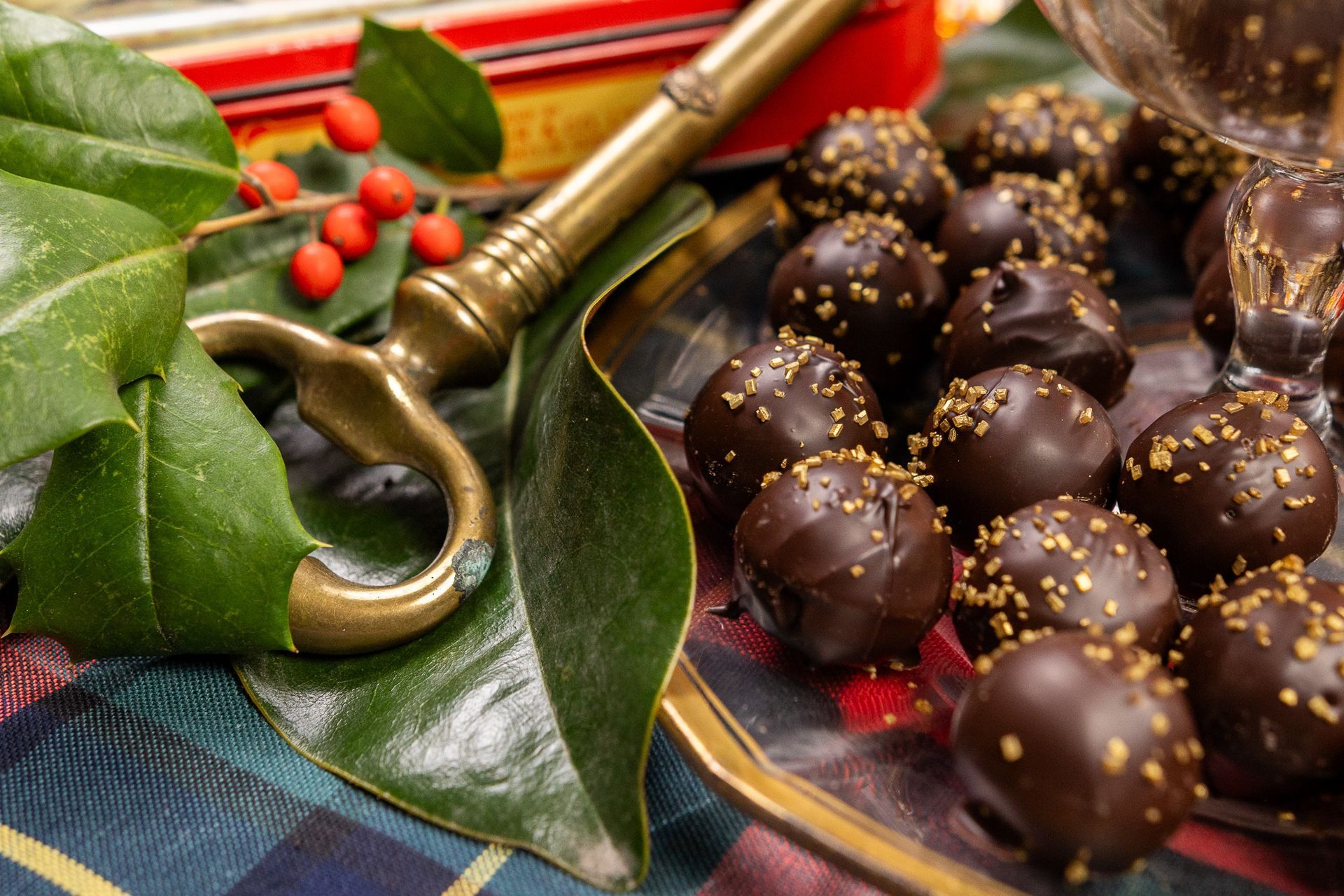 A decorative bowl filled with dark chocolate truffles topped with gold dust, resting near an antique brass key and holly.