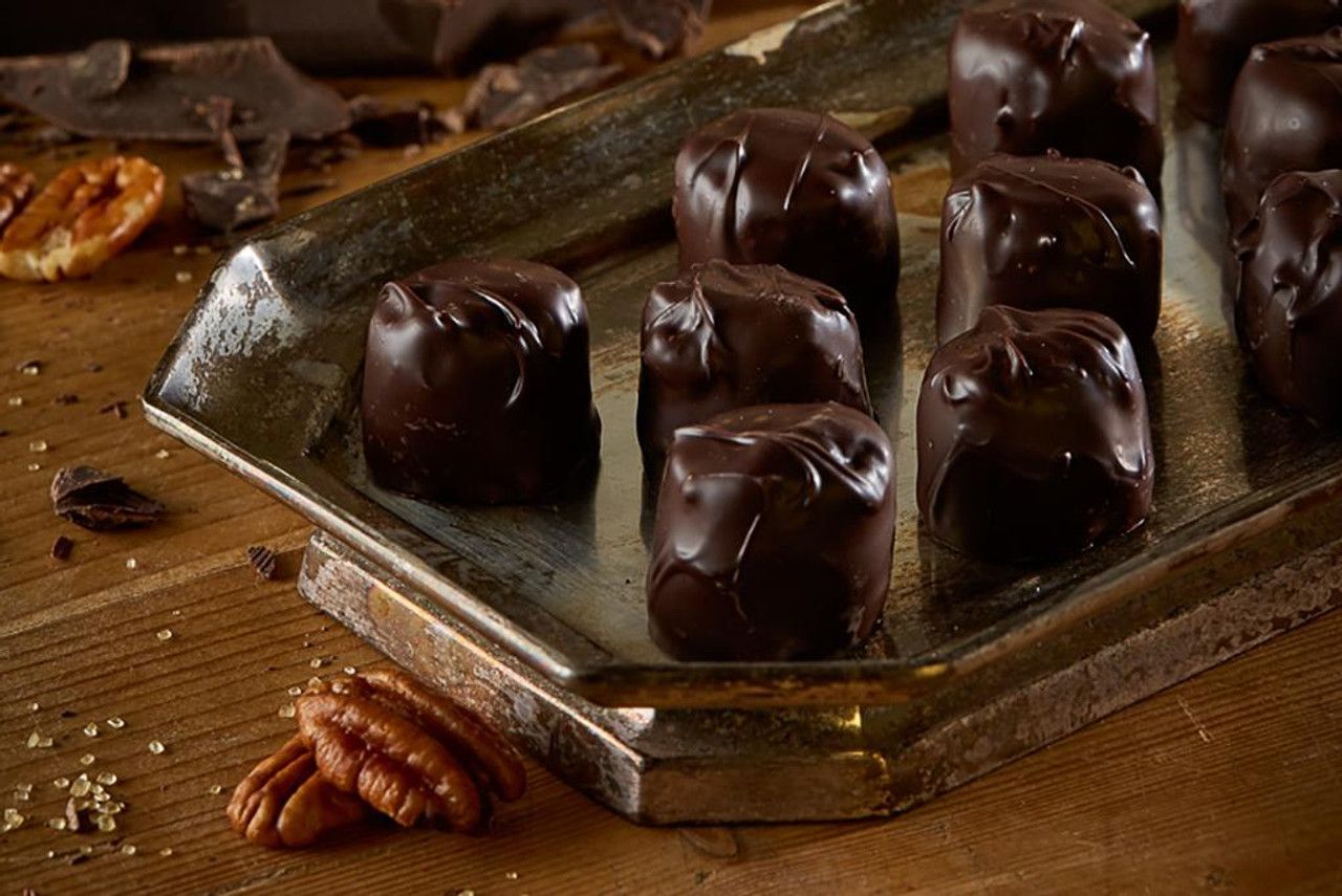 Dark chocolate candies on a silver tray, with pecans and chocolate pieces scattered around.