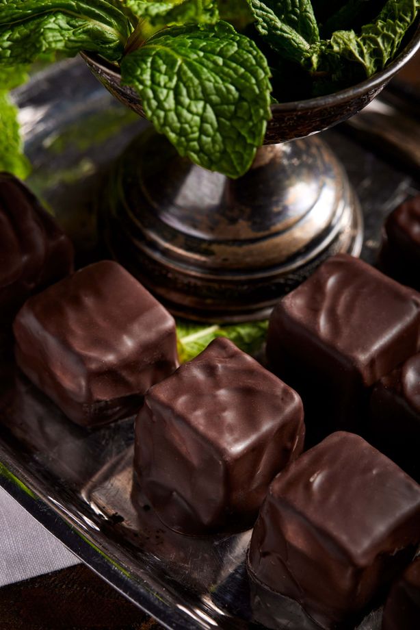 Chocolate mint candies on a silver tray with fresh mint leaves in a silver container.