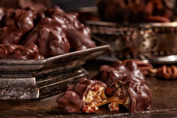 Chocolate pecan clusters, some on a tray. One is cut open, revealing caramel.