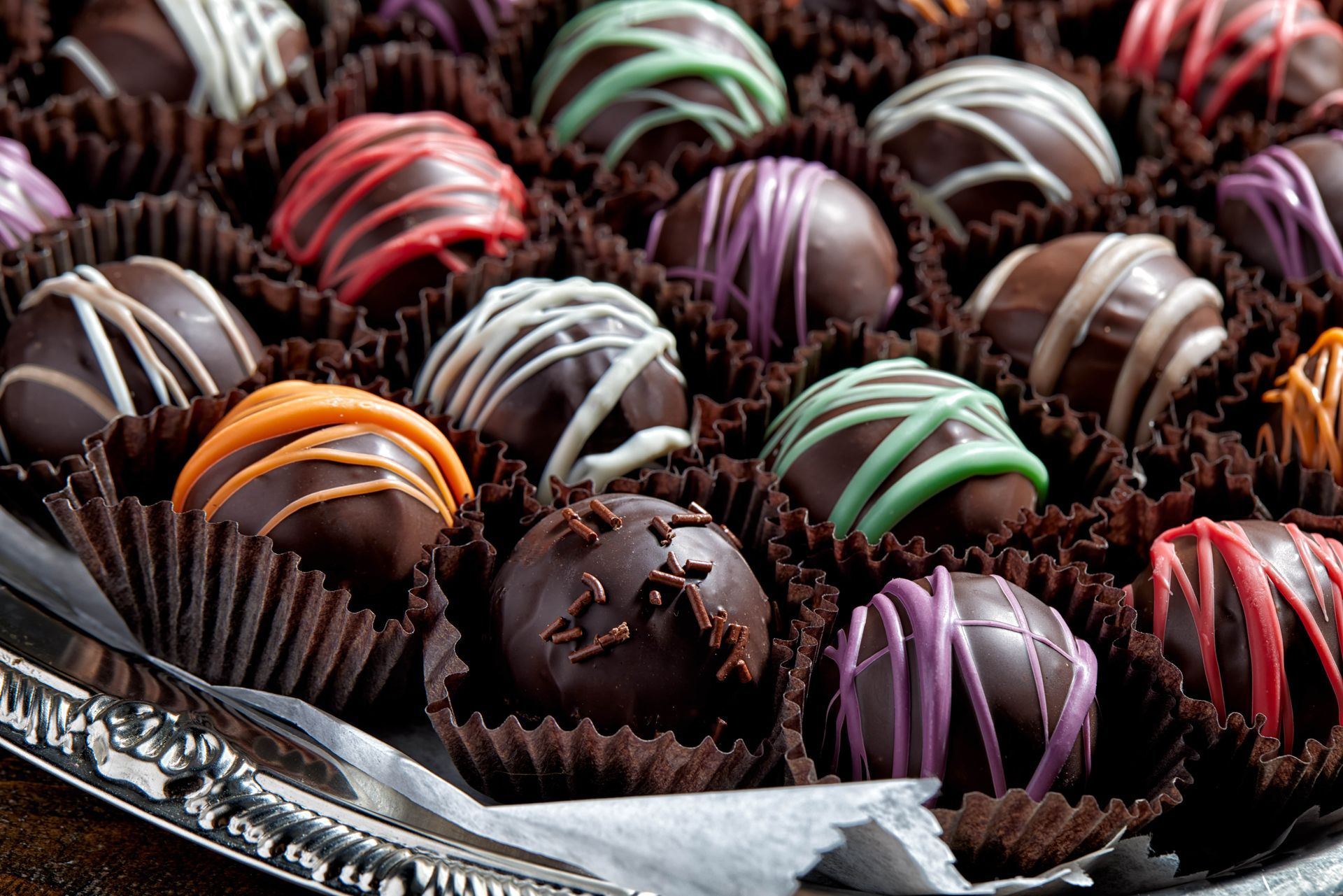 Tray of chocolate truffles, each with colorful drizzle on dark chocolate.
