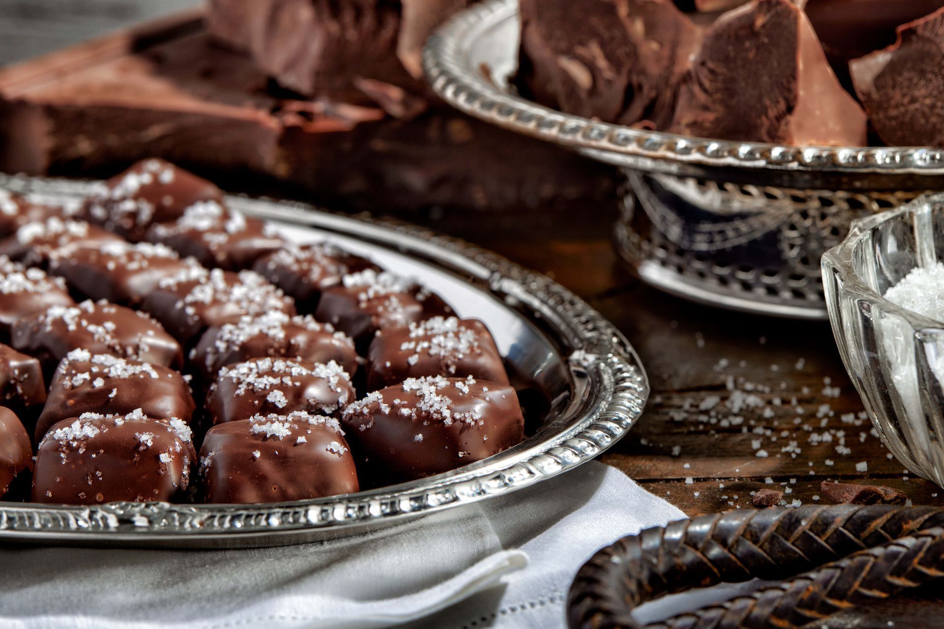 Silver trays of chocolate candies sprinkled with coarse salt. Other chocolate and salt visible.