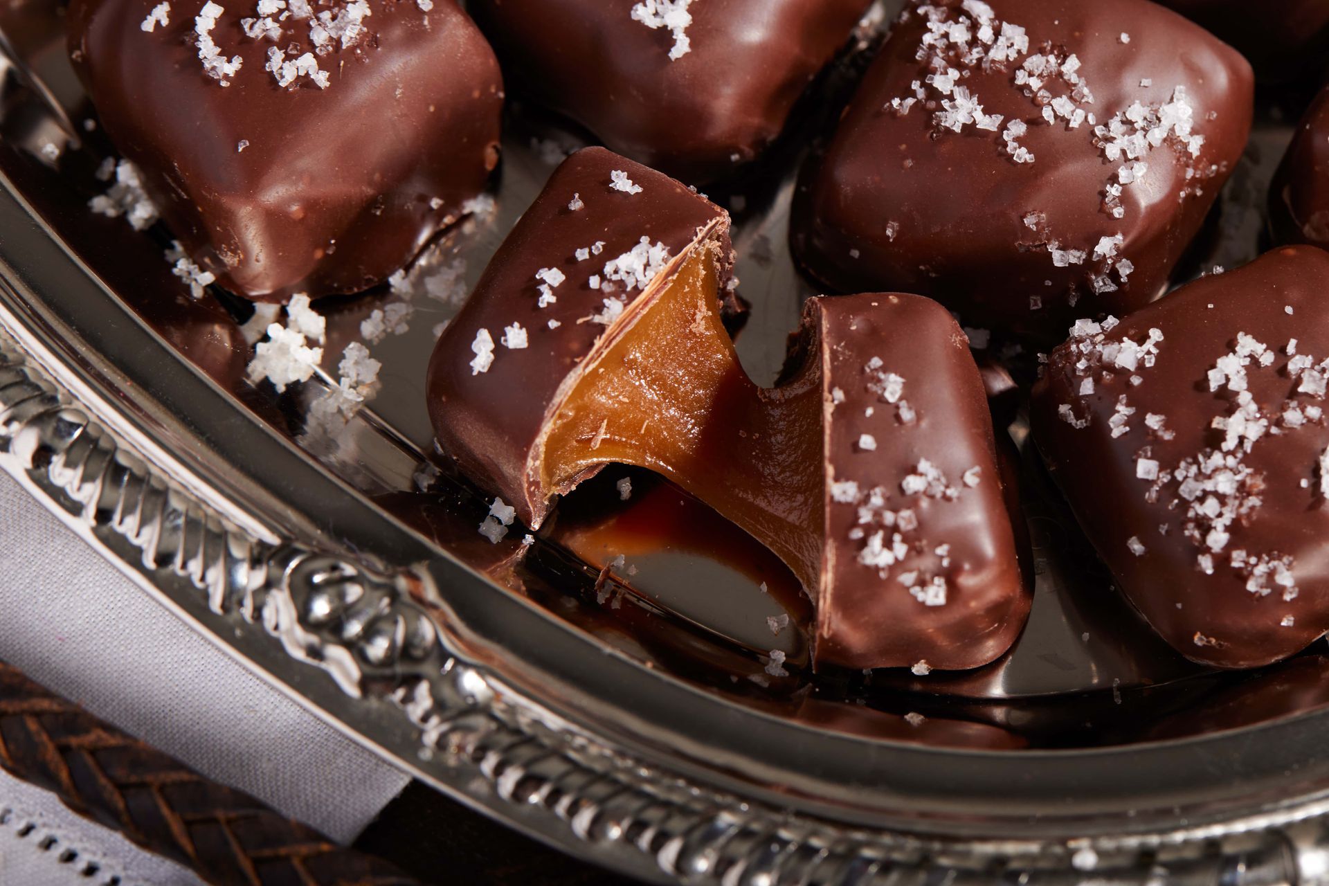 Chocolate-covered caramel candies on a silver platter, sprinkled with sea salt.