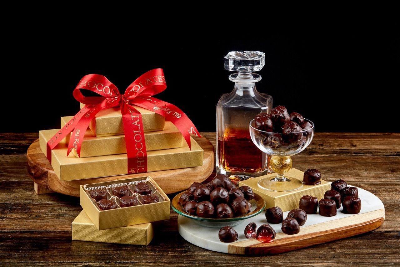 Arrangement of chocolate gifts, liquor decanter, and candies on a wooden table, against a dark background.