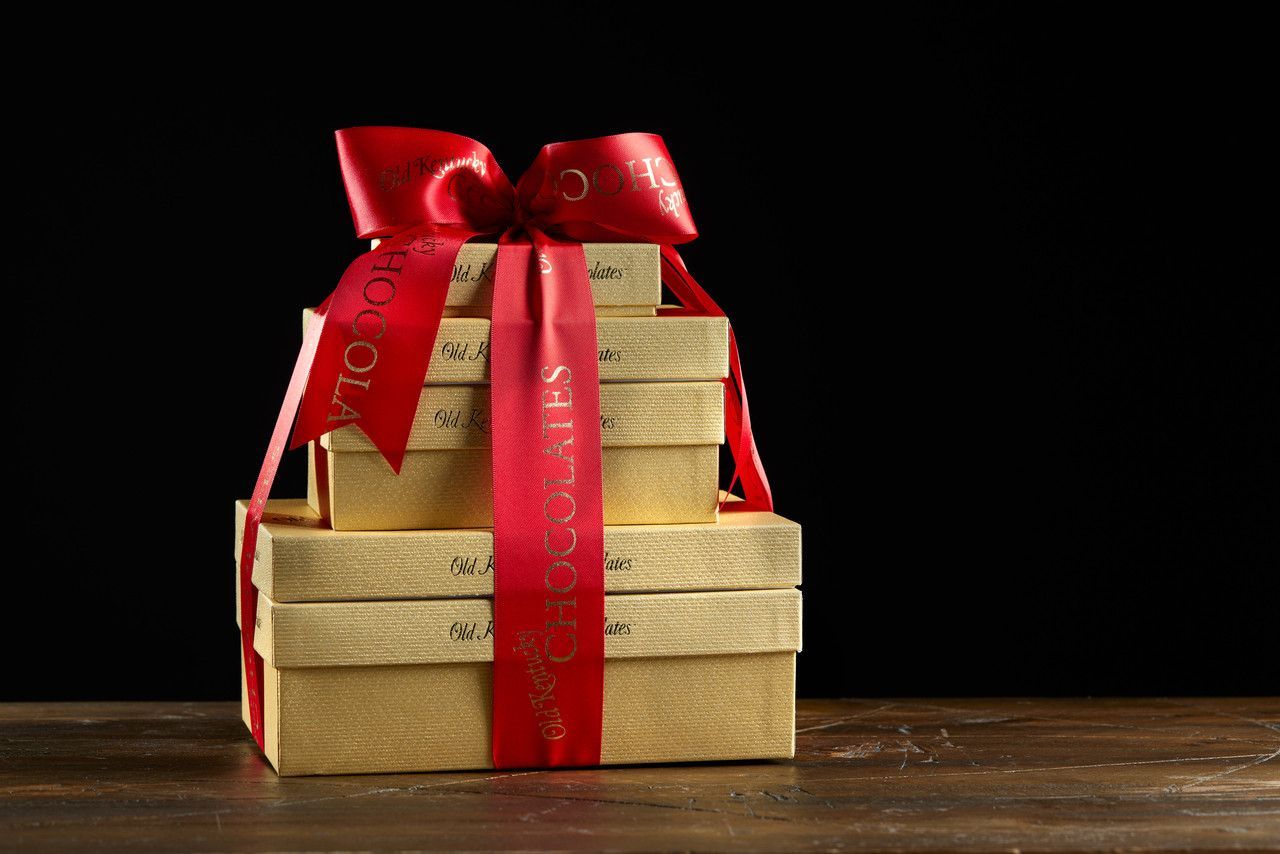 Gold gift boxes stacked, tied with a red ribbon and bow on a wooden surface, set against a black background.