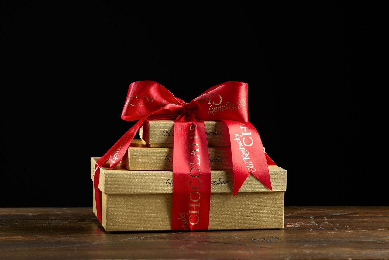 Gift boxes stacked and tied with a red ribbon on a wooden surface. Dark background.