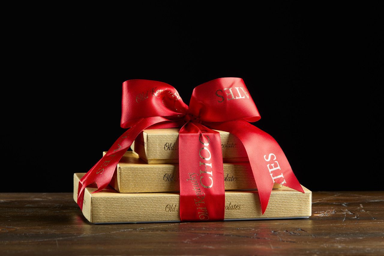 Stacked gold boxes tied with a red ribbon and bow, on a wooden table.