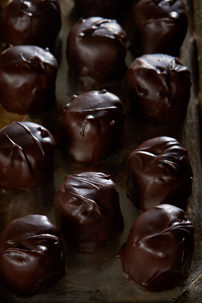 Dark chocolate candies on a silver tray, with pecans and chocolate pieces scattered around.