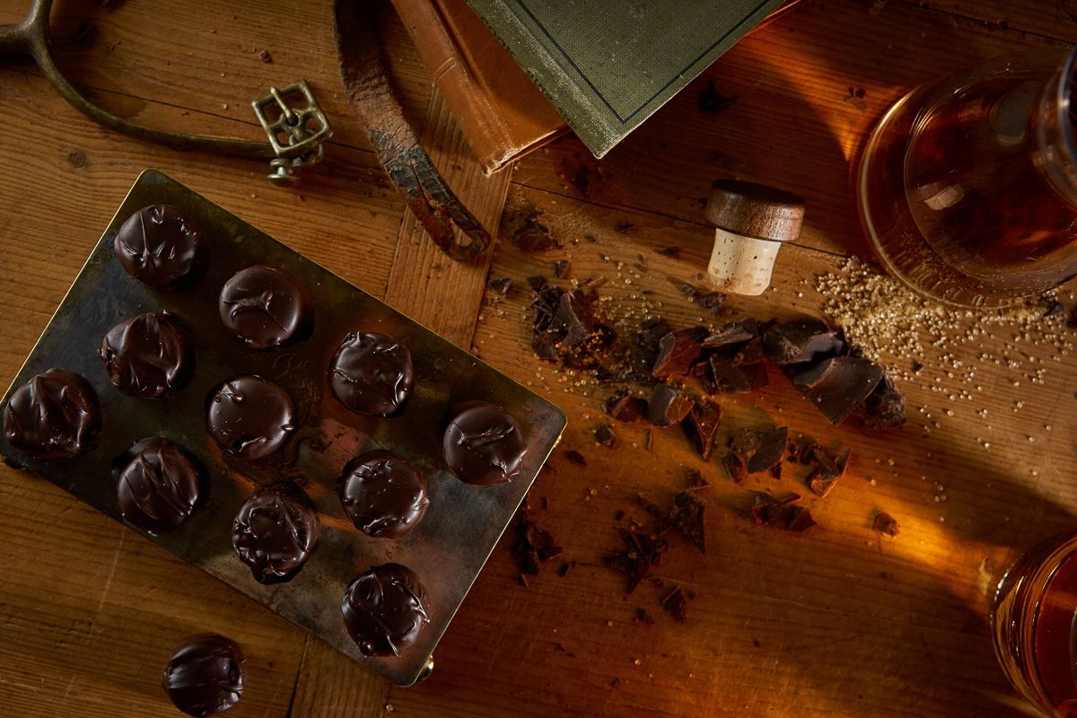 Tray of dark candies, glass bottles, and a book on a wooden surface, with a vintage aesthetic.