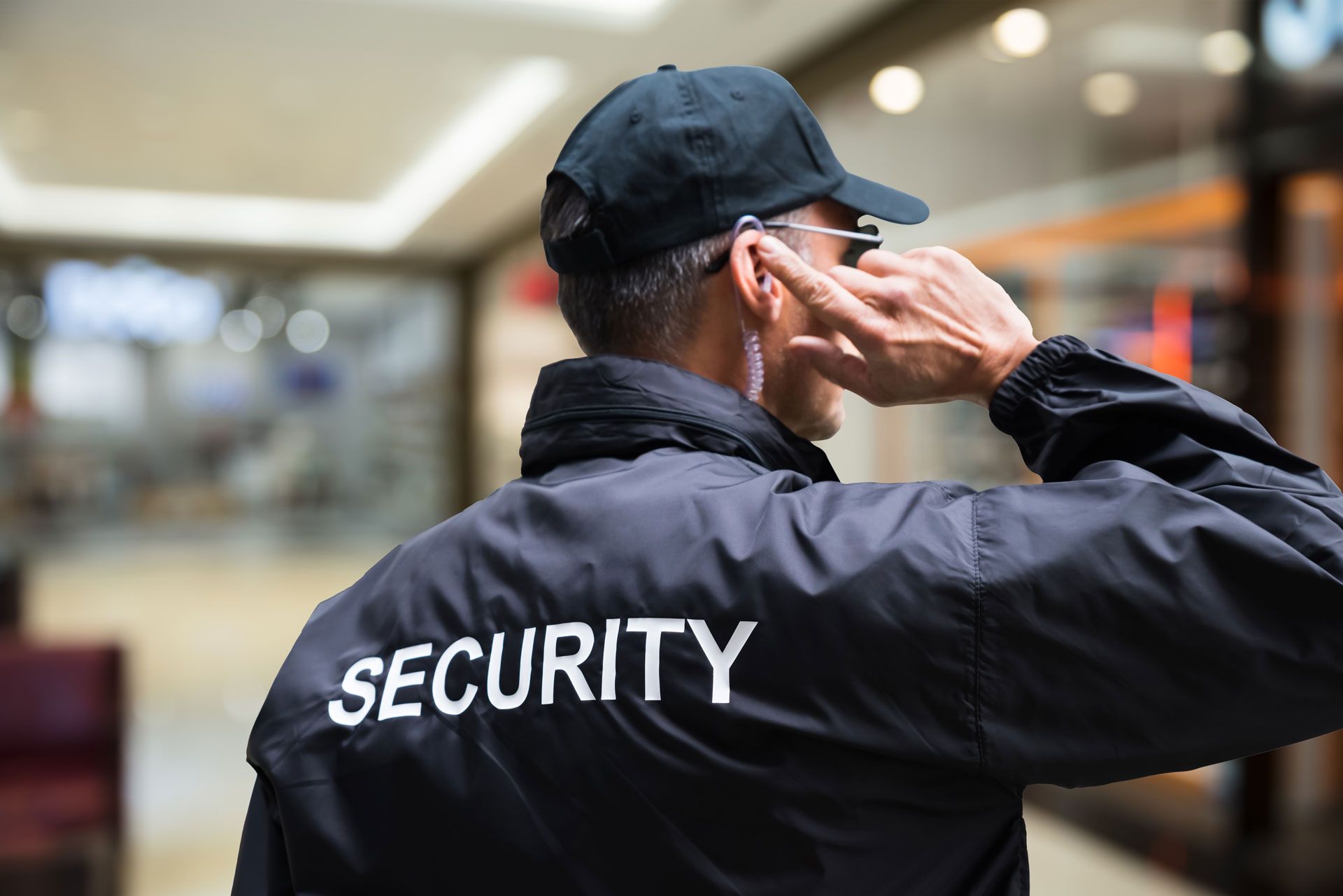 Security guard in black jacket salutes in a blurred indoor setting