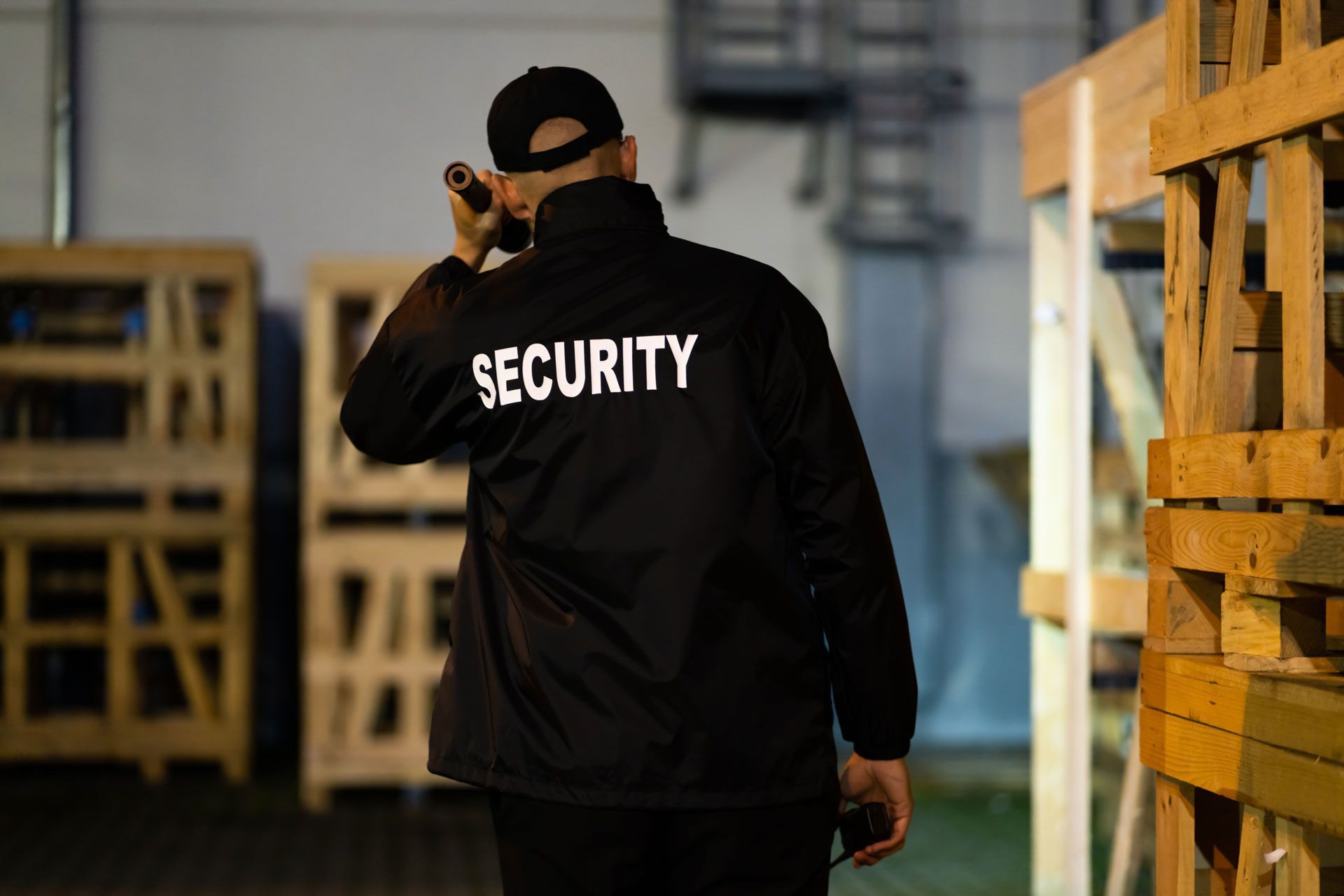 Security guard in black jacket with “SECURITY” on back, walking through a warehouse aisle.