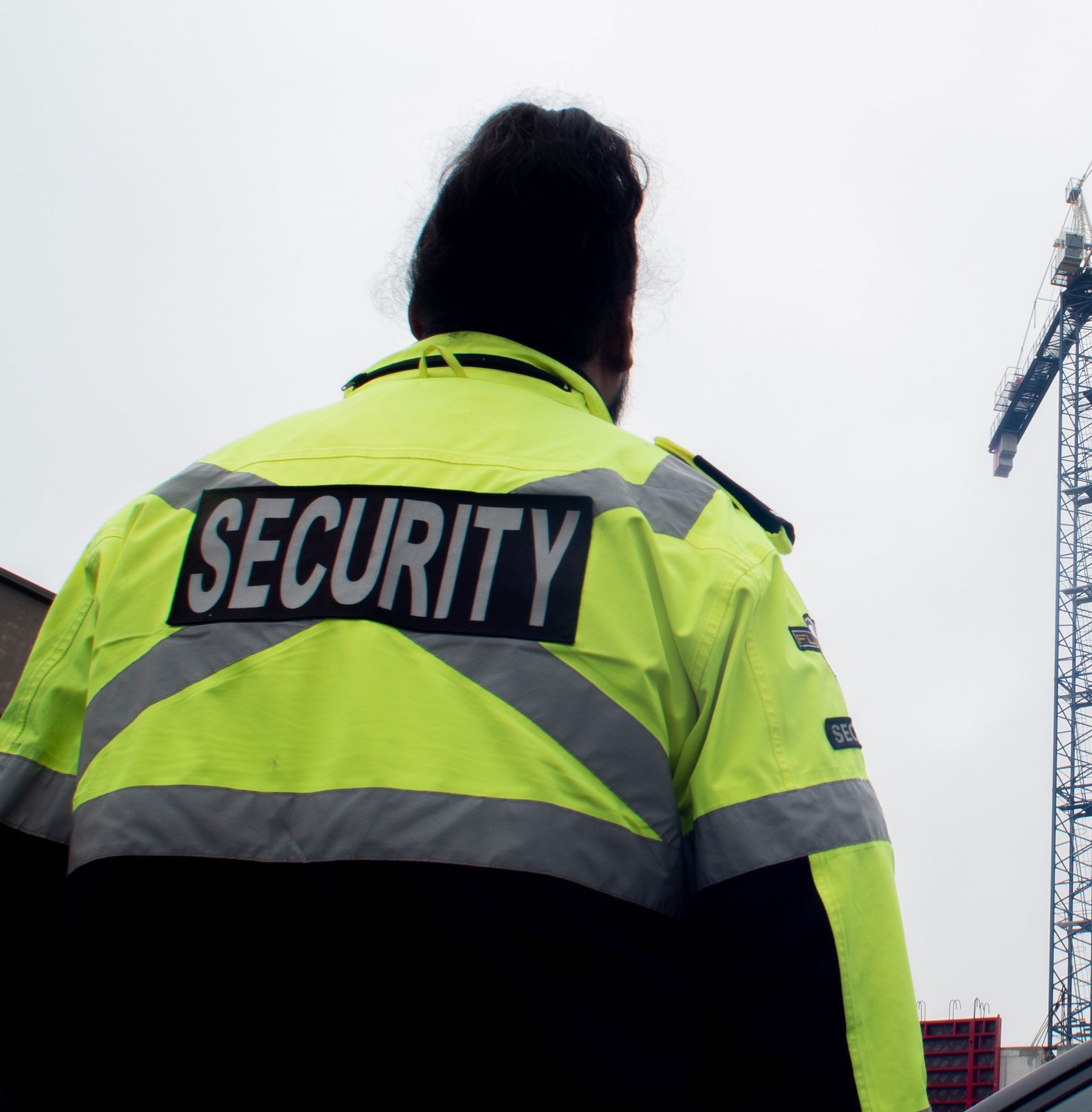 Security guard in a neon yellow jacket seen from behind at an outdoor site