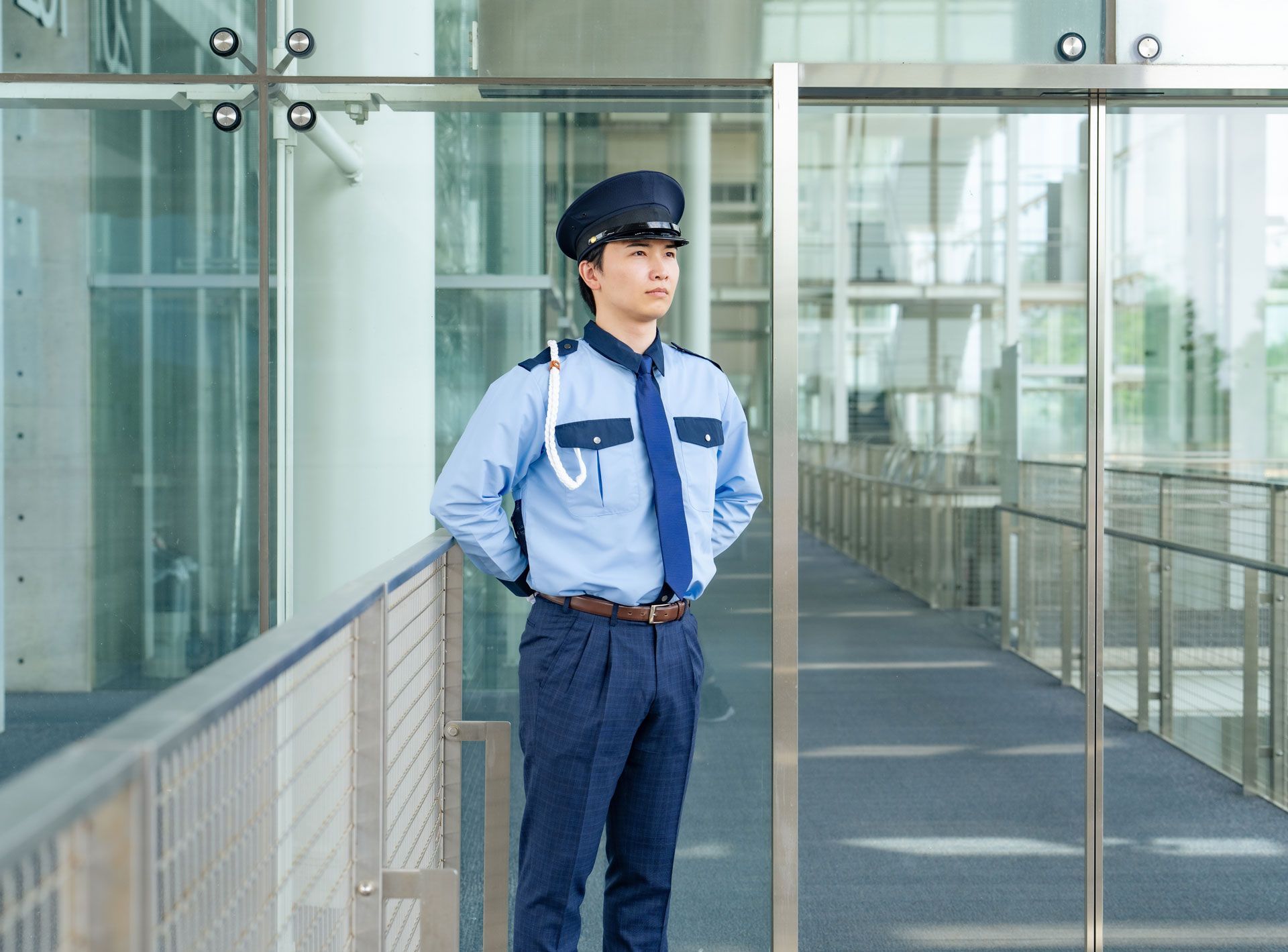 Security guard standing in a glass-walled corridor with hands clasped behind his back