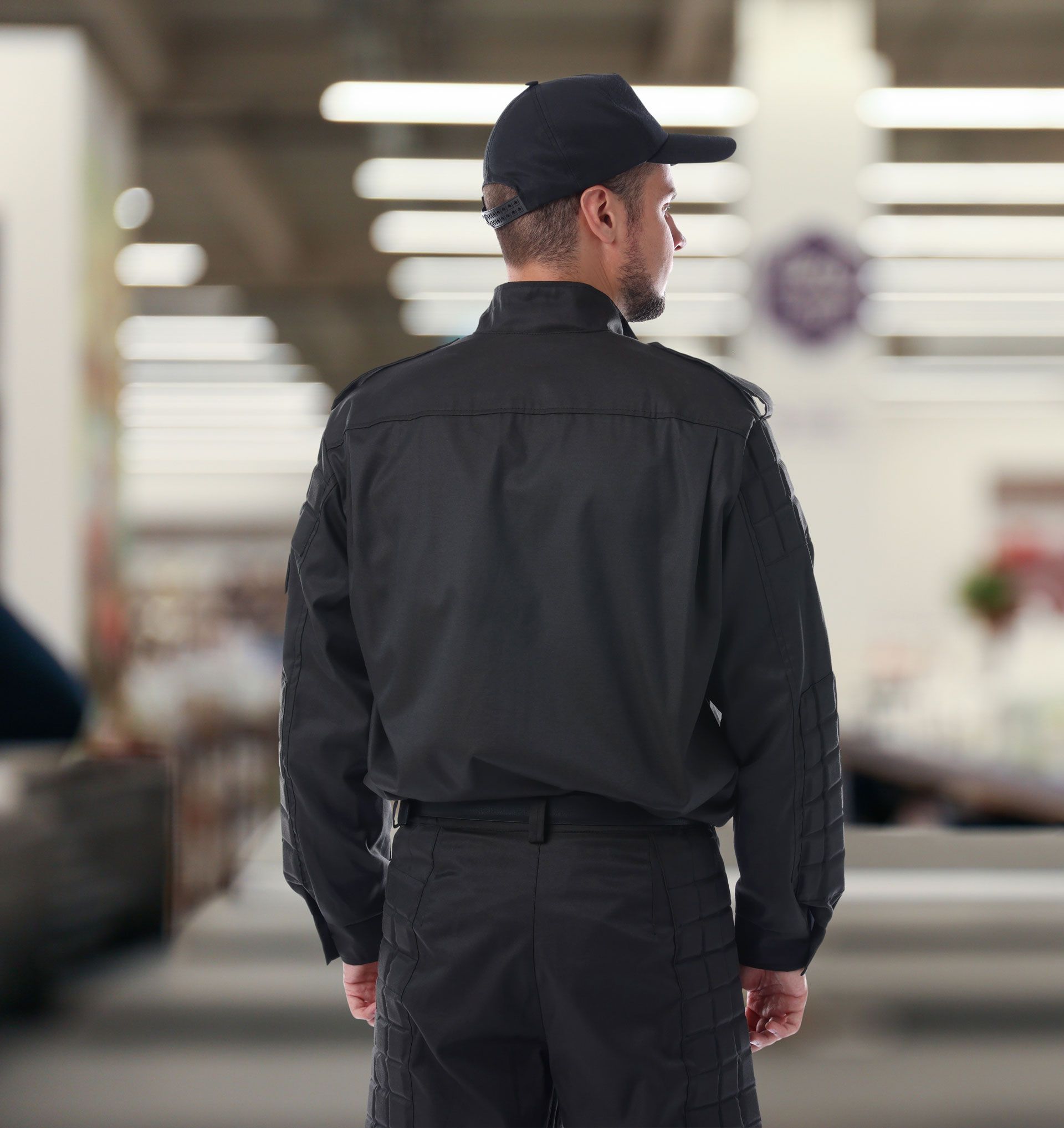 Black-clad security guard standing indoors with his back turned in a blurred public space