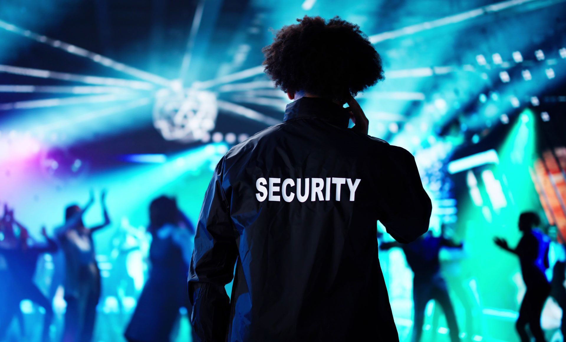 Security guard facing a blue-lit concert crowd, with bright stage lights in the background