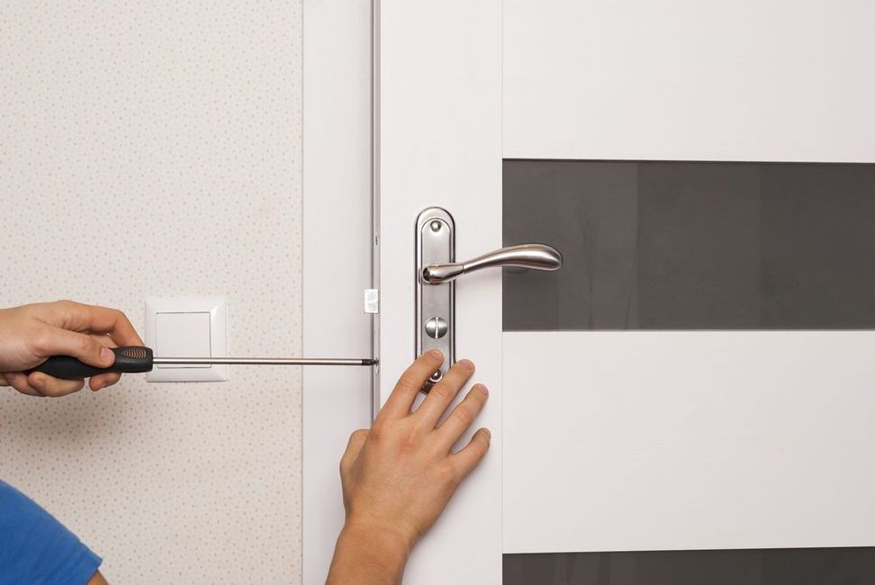 A person is fixing a door handle with a screwdriver.