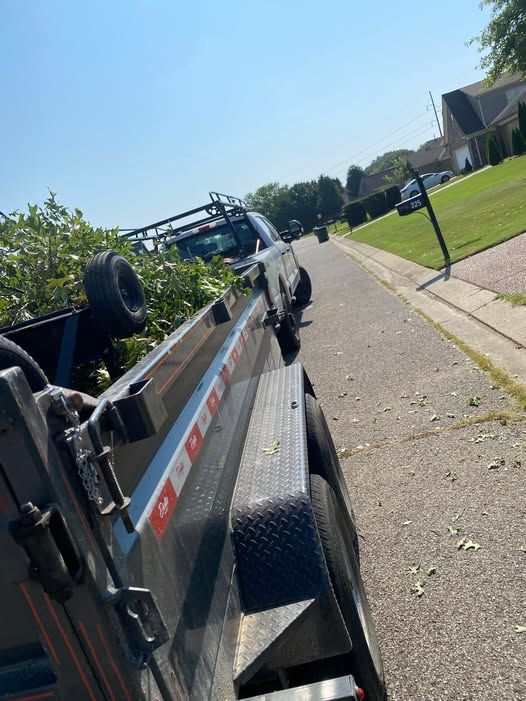 A white pickup truck with a trailer filled with branches parked on a residential street on a sunny day.