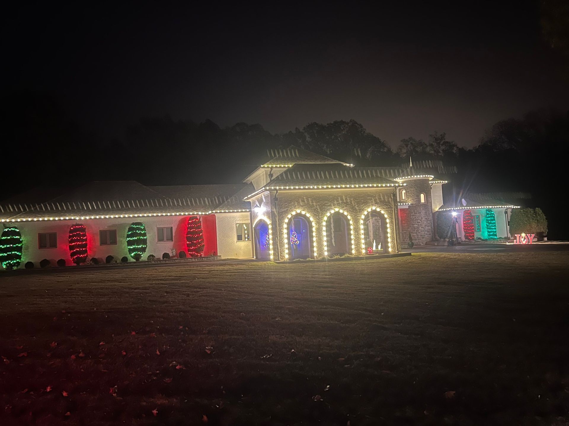 A large house at night is decorated with Christmas lights in red, green, and white.