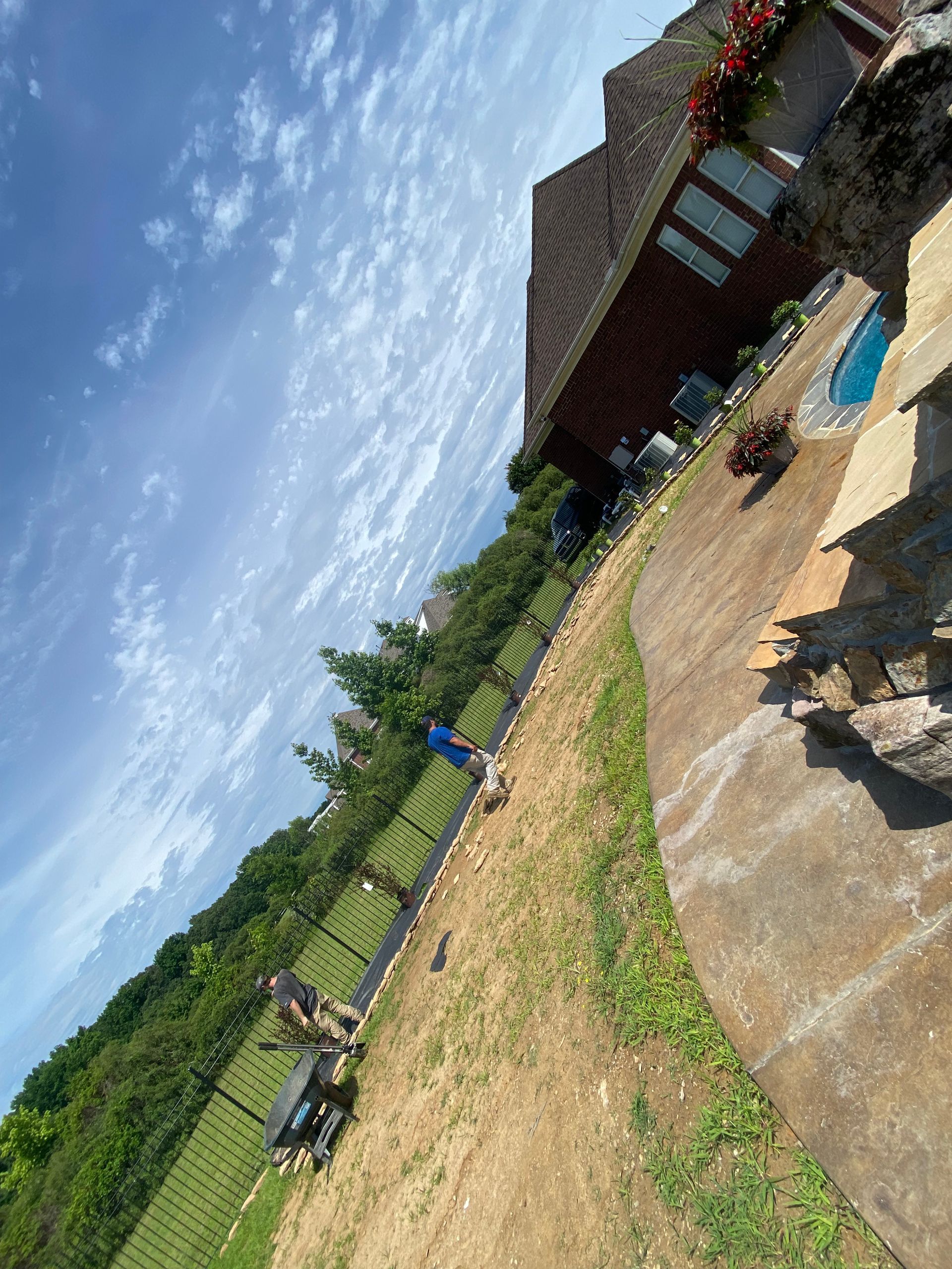A tilted outdoor scene with a house, a pool, and a grassy yard. Two dogs play near a fence, and a person stands in the yard.