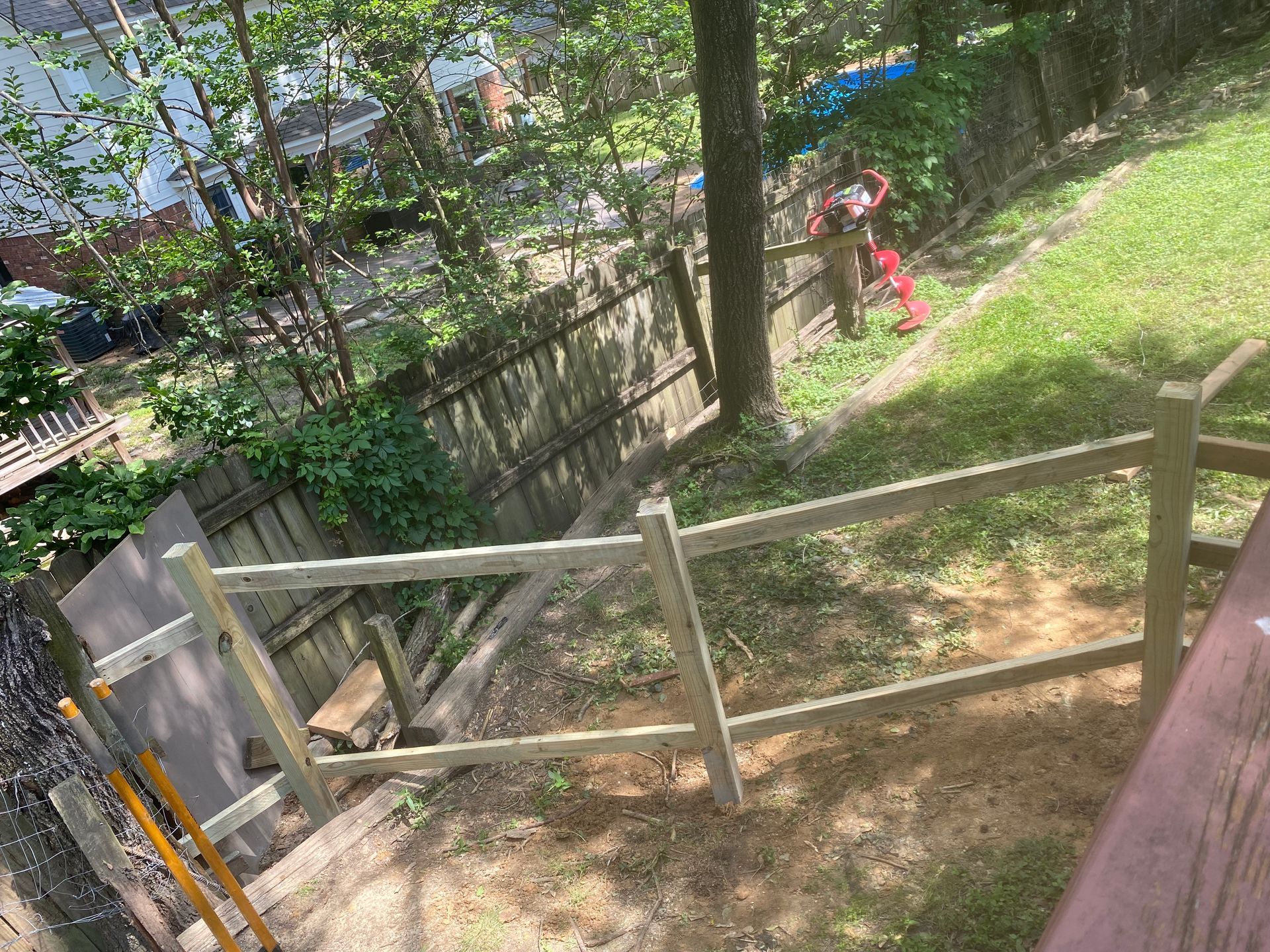 A split-rail fence is being built in a backyard with a wooden deck and a grassy slope.