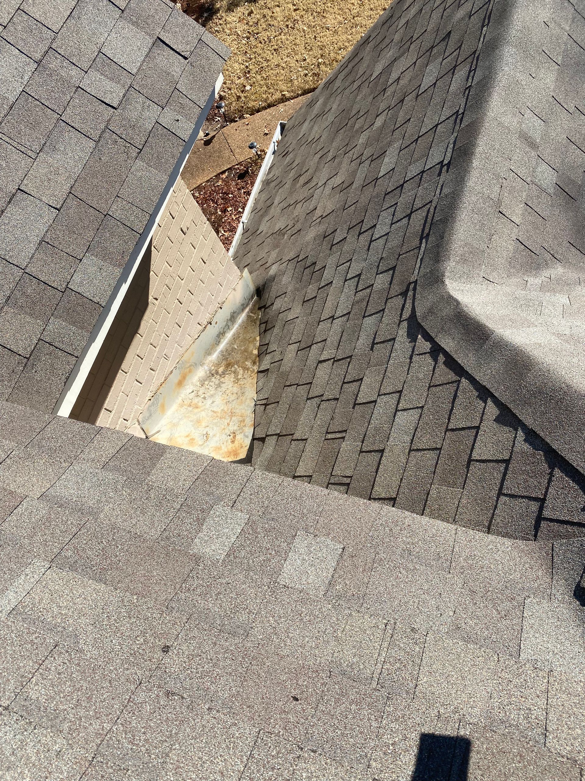 Overhead view of an asphalt shingle roof with algae growth. A section of the roof shows a gap where shingles are missing.