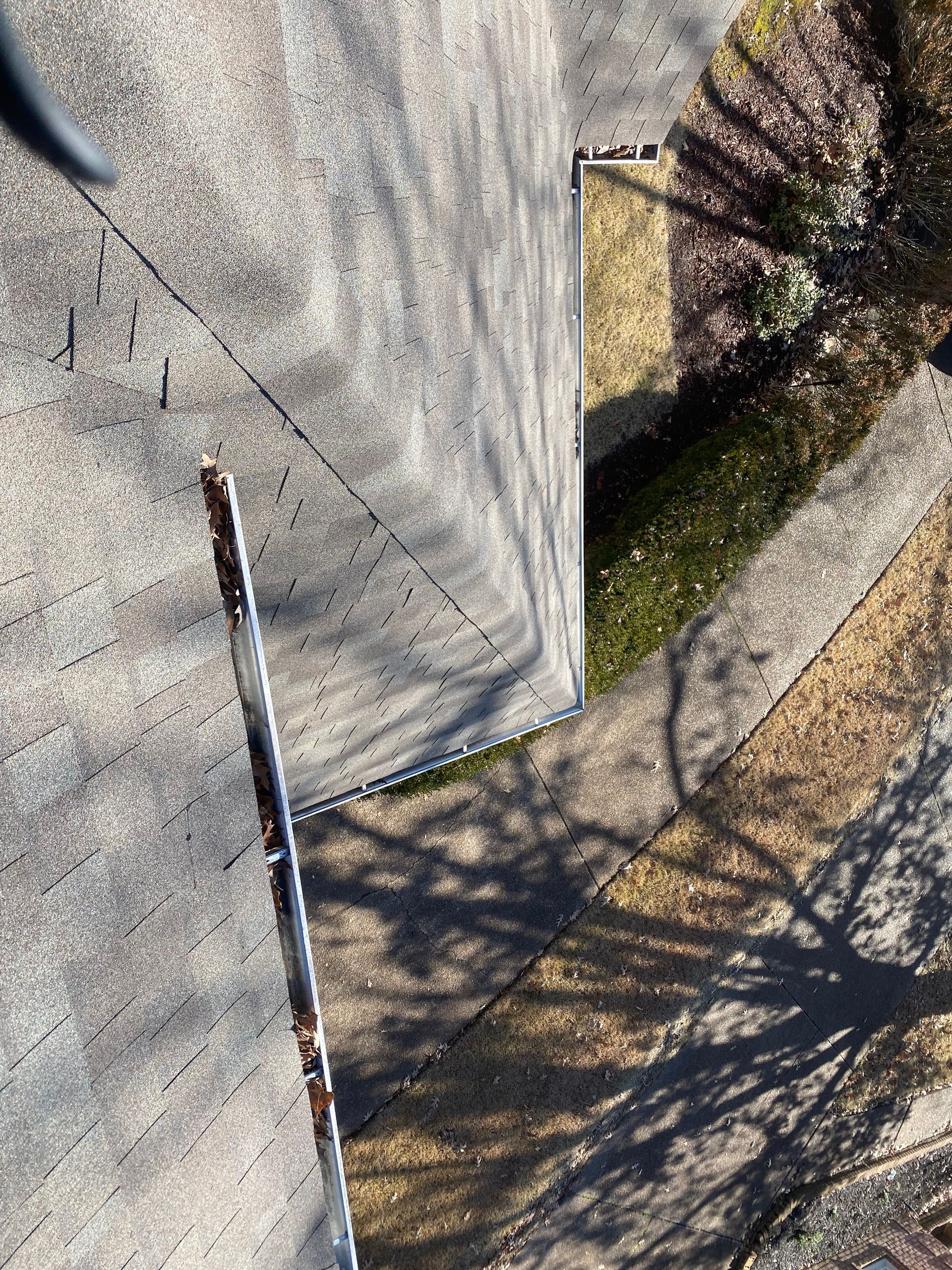 Overhead view of a house roof with a rusty gutter, a small green hedge, and a sidewalk with shadows from trees.